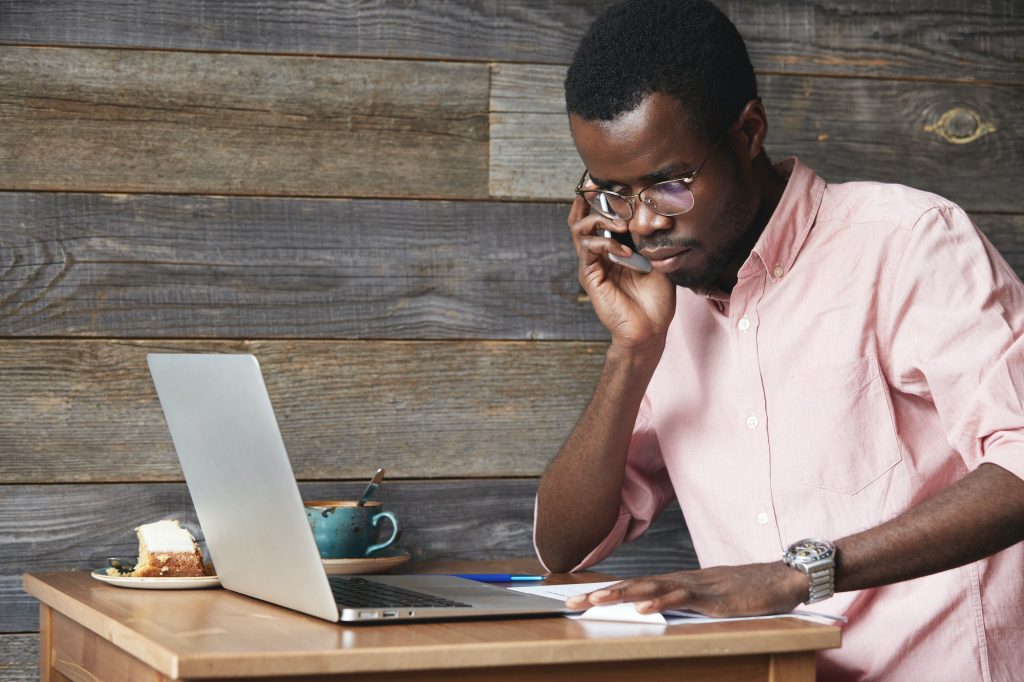 Profile portrait of young African online shop manager, talking on mobile phone to client, consulting